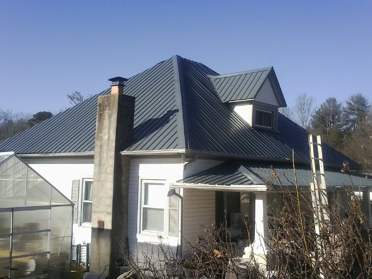Dark blue standing seam metal roof on a white farmhouse with dormer — Slate & Tile Roof Repair by Roofing Brothers in Piney Creek