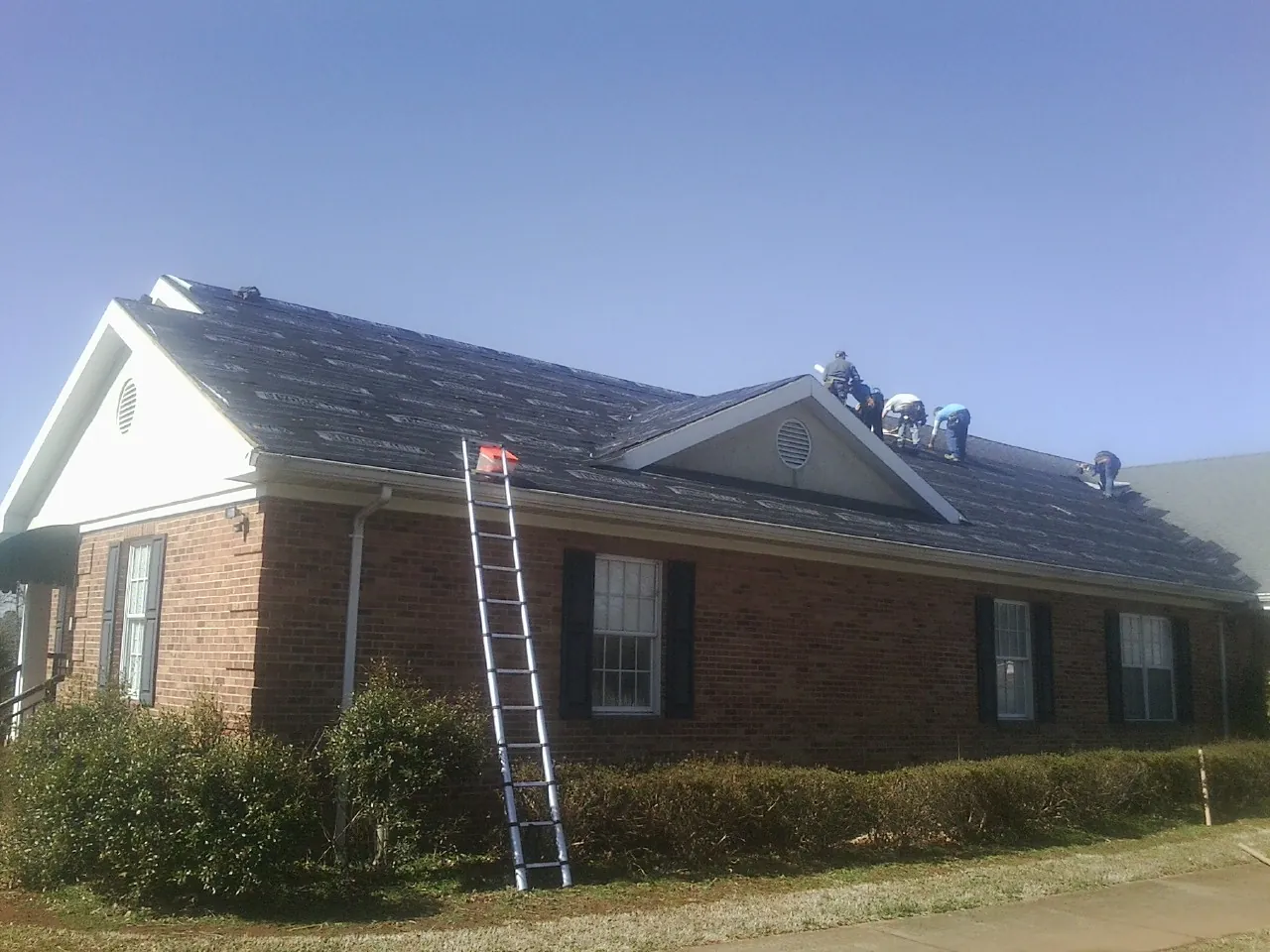 Crew tearing shingles off a brick ranch roof with a ladder set — Emergency Roof Repair work by our crew in Piney Creek