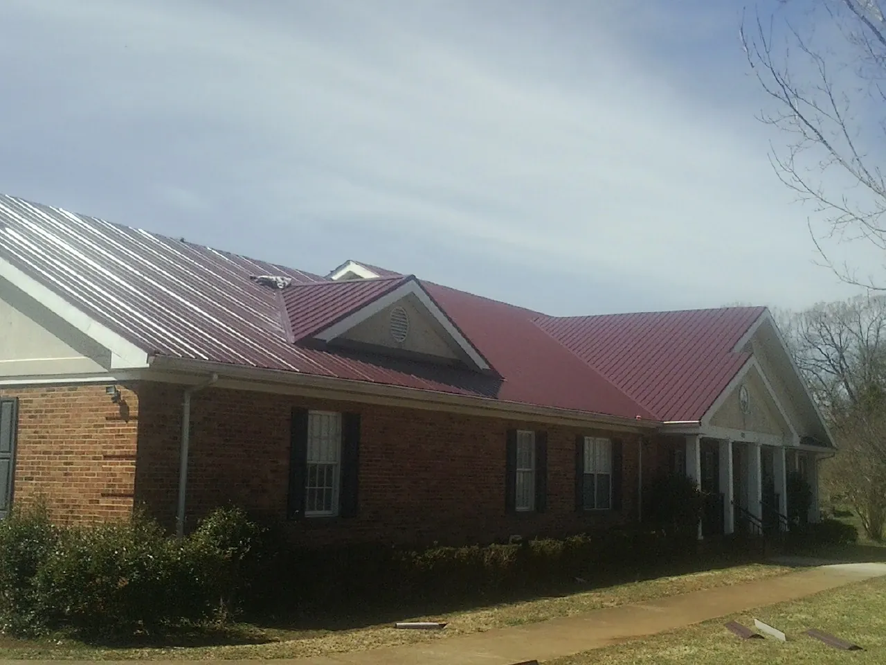 Red metal roof with gabled entries on a long brick building, from a Hail Damage Roof Repair job in Piney Creek