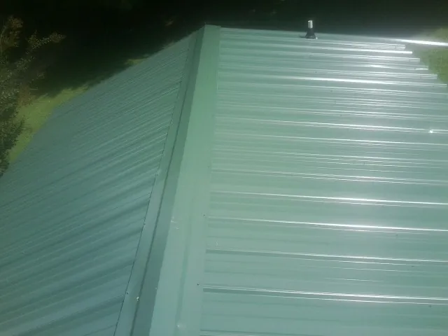 New green metal panels meeting at the ridge of a roof — Flat Roof Repair work by our crew in Piney Creek