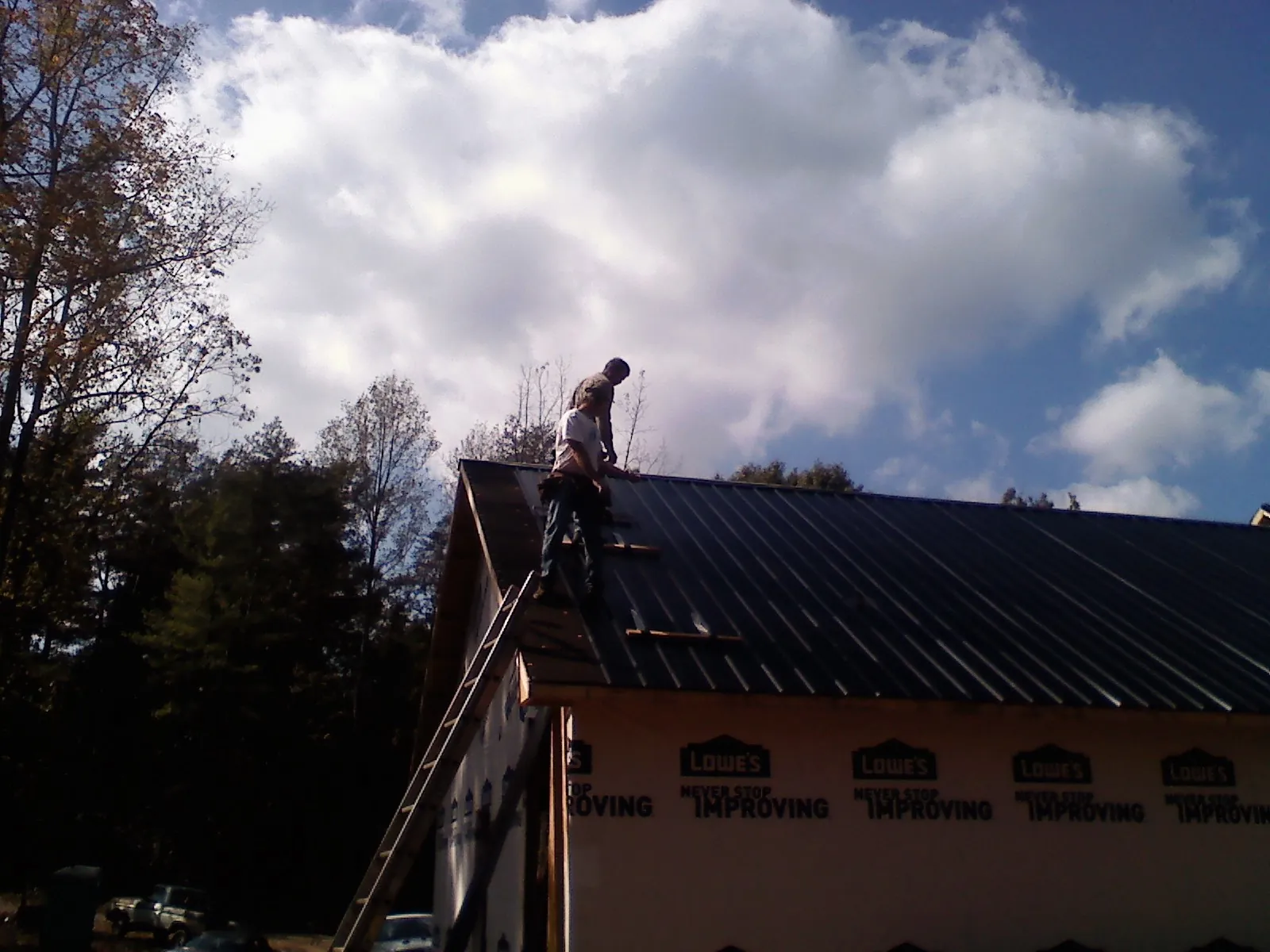 Roofer fastening dark metal panels high against a cloudy sky, from a Roof Inspection job in Piney Creek
