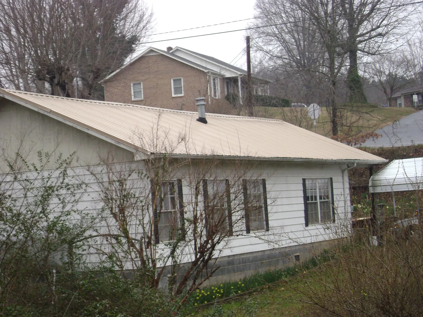 Tan metal roof on a white sided house set into a hillside — Commercial Roofing by Roofing Brothers in Piney Creek