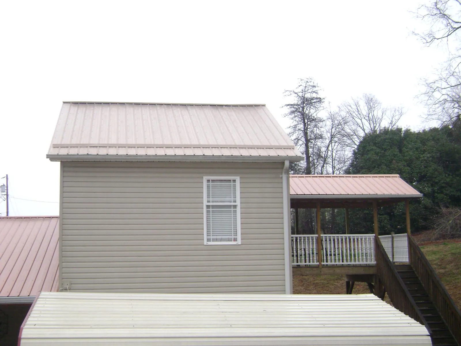 Tan metal roofs on a two story addition and attached porch, from a Roof Replacement job in Piney Creek